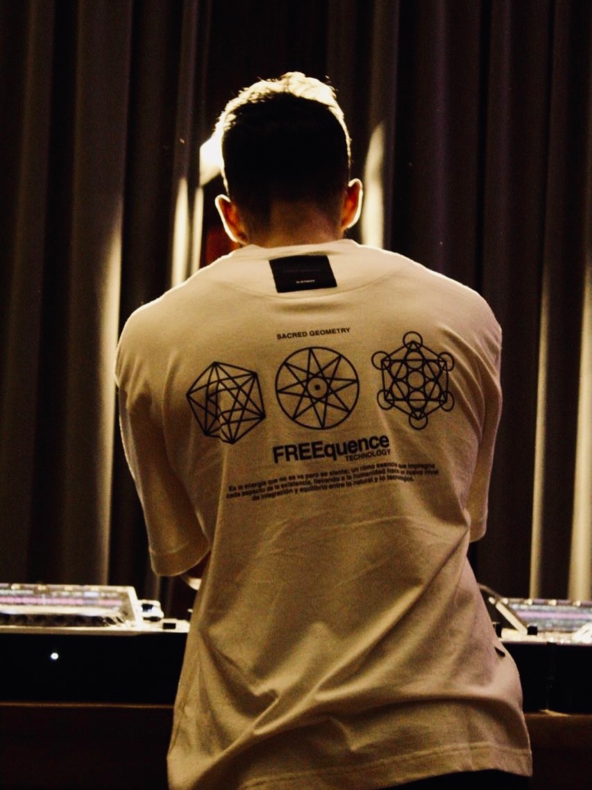 BROD DJ de espaldas en cabina de mezclas con remera Sacred Geometry